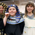 Two young boys and a girl dressed up in Egyptian costumes in front of the mummy in the Unearthing Ancient Egypt exhibit while on a field trip at the Putnam Museum.