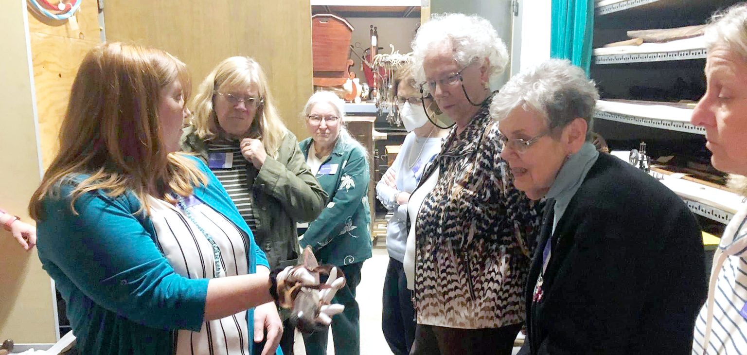 Members of the Putnam Guild viewing an artifact with a museum curator in the museum collection.
