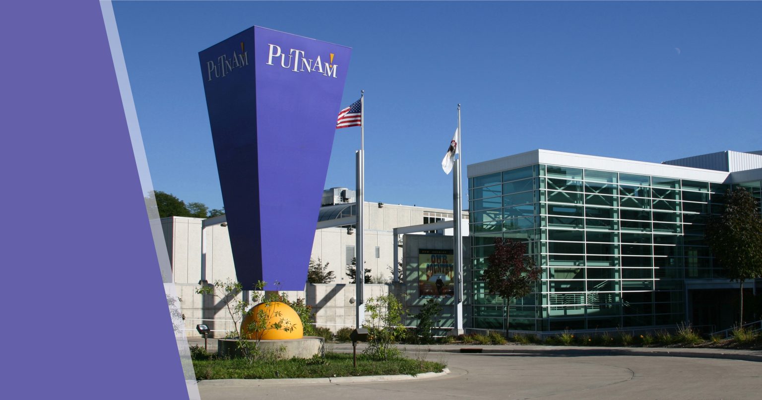 Exterior of Putnam Museum featuring iconic exclamation point statue and sign. Modern industrial architecture of the Grand Lobby with American flag flying against a cloudless blue sky.